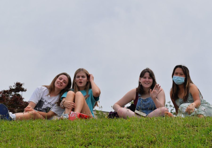 Juniors Elizabeth Jackson (left), Sadie Hathaway (middle left) , Maddie Colavincenzo (middle right), and Vivian Hui (right) group together on the grassy hill above the tennis courts to cheer on players  during their second block. 