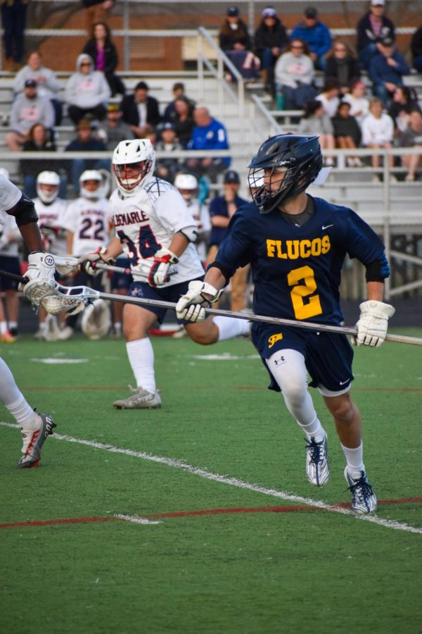 Fluco defender sprints down the field carrying the ball in the pocket of his deep pole. Sophomore Ilhan Doran (34) approaches in the background. 