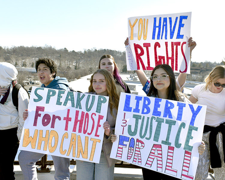 Students display homemade signs behind the Shops at Stonefield.